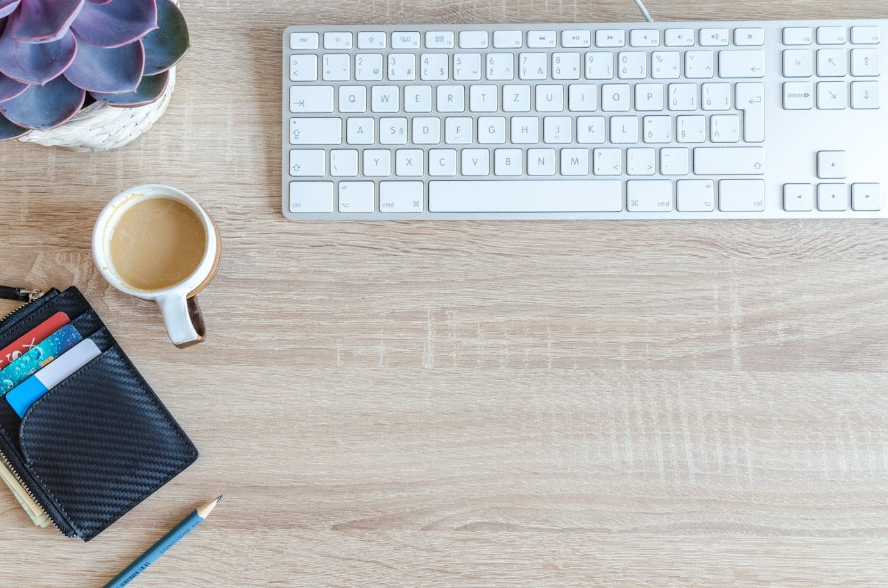 An organized workspace with a keyboard, coffee cup, wallet, and succulent plant on a wooden desk.